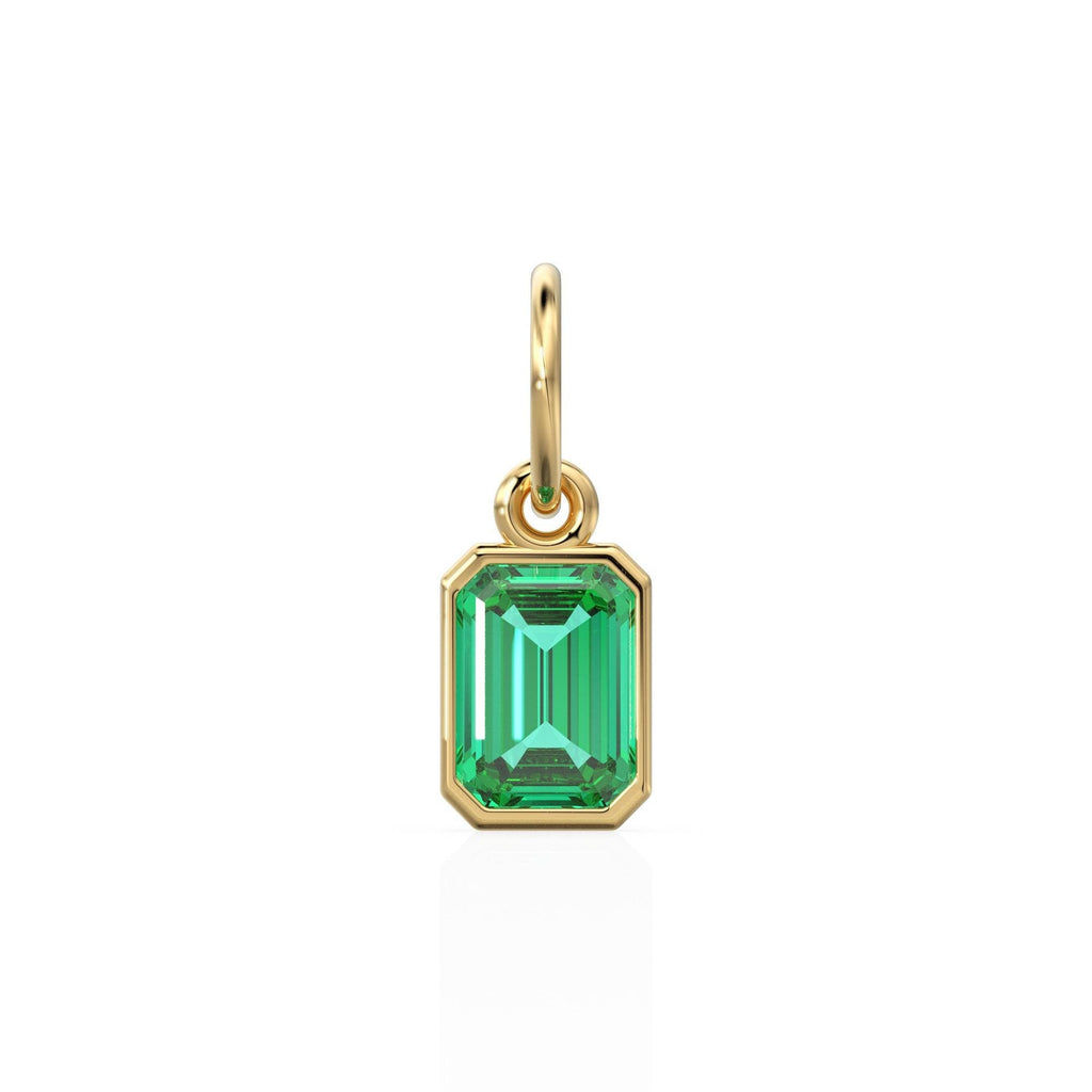 May include: A gold pendant charm featuring a green emerald gemstone in an emerald cut setting.